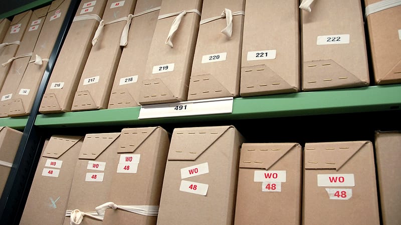 A tall stack of tabbed paper exhibits bound with a large binder clip standing on the corner of a desk