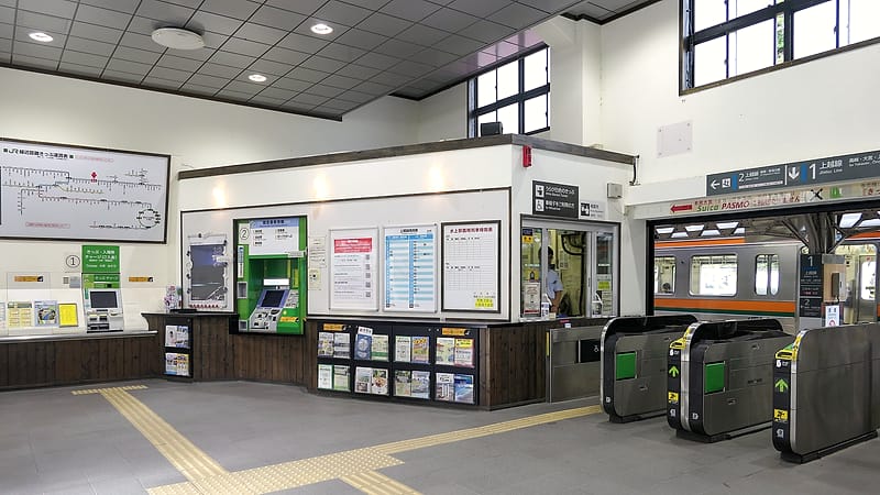 A fare gate array and a validator post inside a transit station concourse with commuters passing through