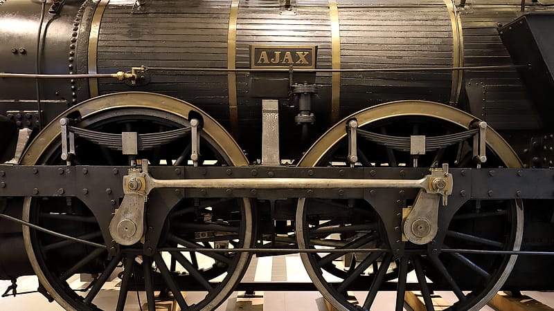 Close view of a knuckle coupler and air hose joining two freight cars, with grab irons and a ladder above