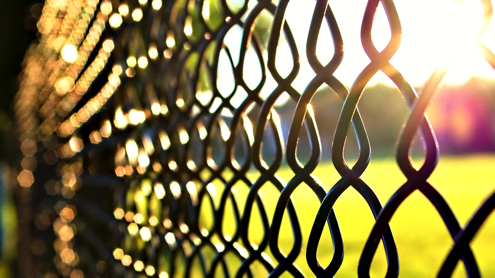 A tall chain link fence topped with coiled wire against a flat overcast sky above a paved empty yard