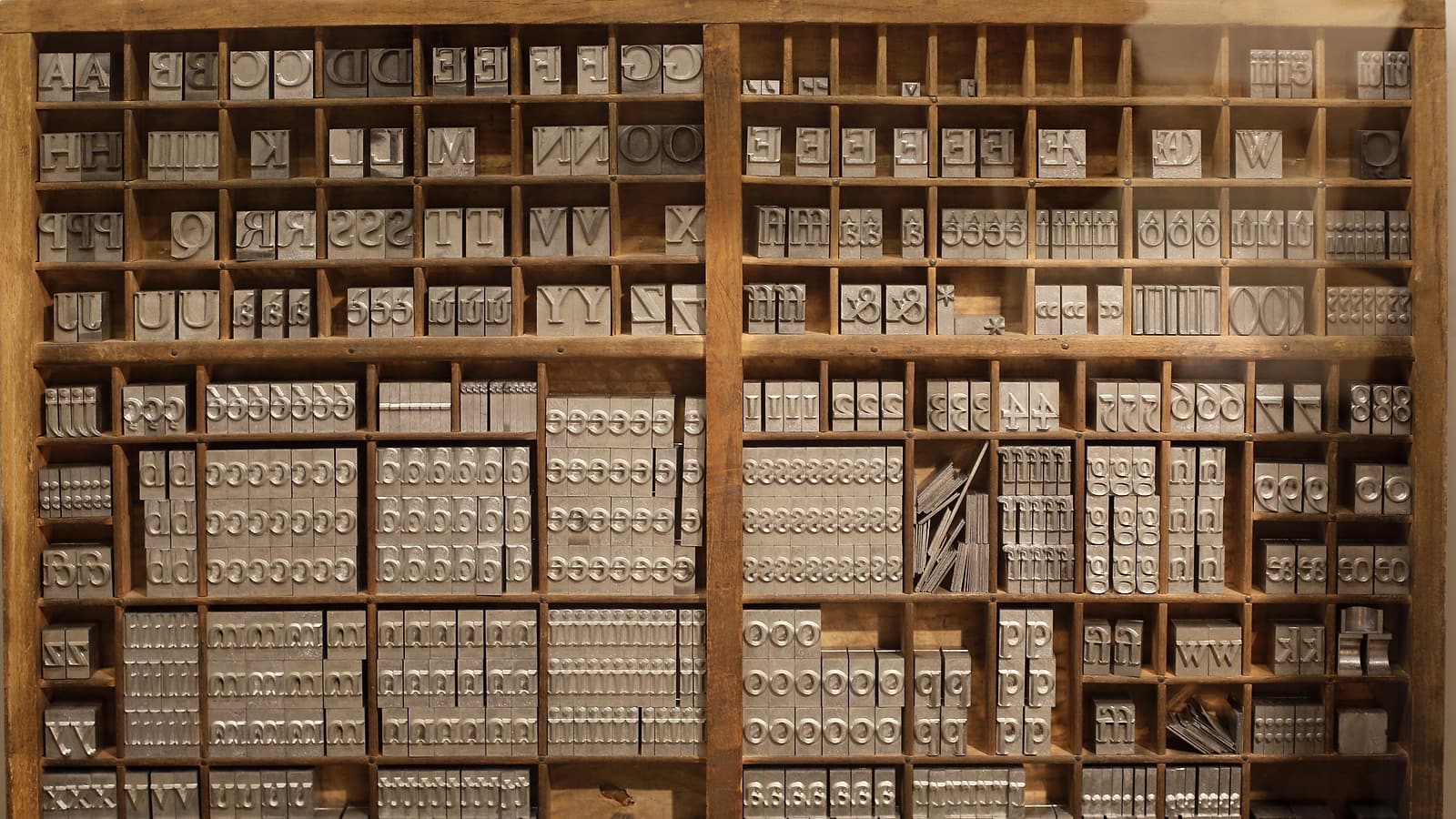 A gray archive box with its lid removed on a metal shelf, holding upright folders with handwritten paper tabs