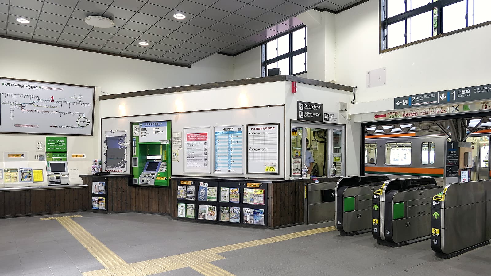 A fare gate array and a validator post inside a transit station concourse with commuters passing through