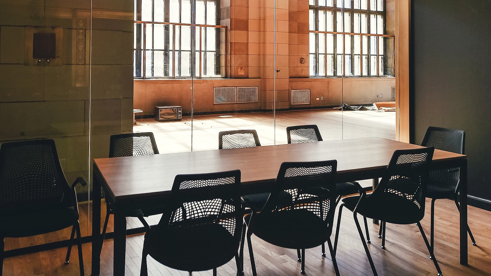 An empty wooden bench and a plain lectern in a bare public hearing room lit by two tall windows