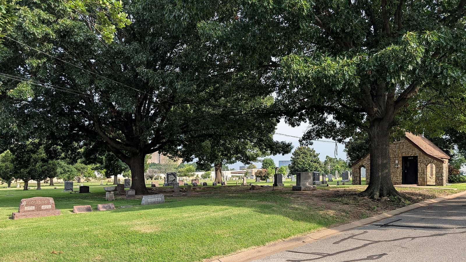 A mown cemetery lawn with flat bronze markers set flush with the grass and a line of mature trees along the far edge